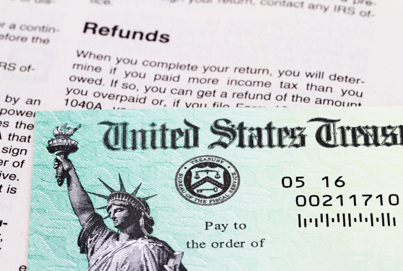 Partial view of a USA Treasury Internal Revenue Service tax refund check showing the Treasury seal and image of the Statue of Liberty. The IRS tax refund check lies on a page of a IRS booklet which explains how to file a tax return.
